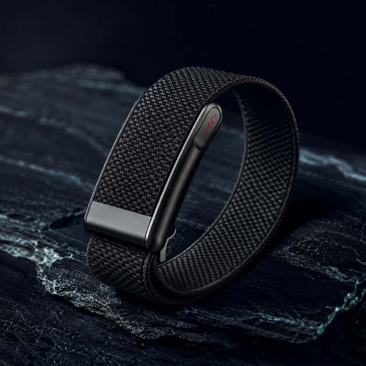 The GLP Care Band — a screenless woven band with a metal clasp, resting on dark stone